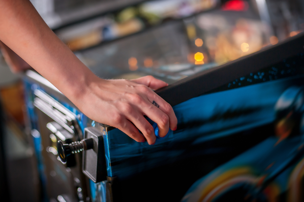 hands and arms next to a pinball machine, the person is about to start playing the machine