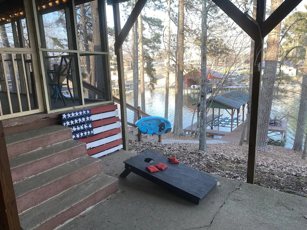 view of the screened in porch, cornhole game, and dock of the lakeside cabin in Alabama