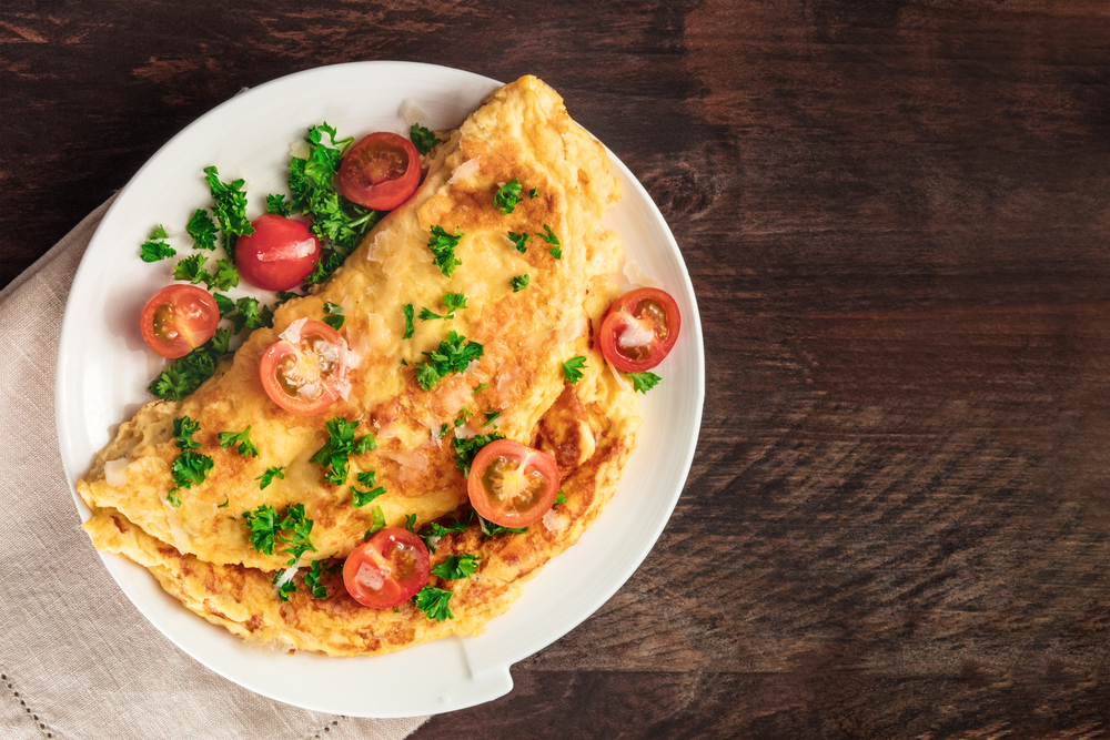 photo of an omelette with tomatoes on a white plate on a dark wooded table background
