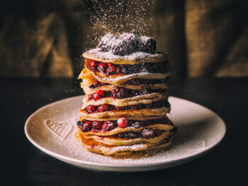 photo of a stack of pancakes with fruit and powdered sugar