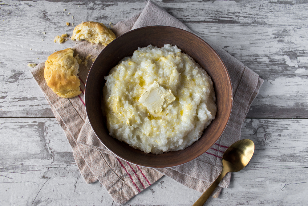 photo of a bowl of grits with a knob of butter next to a broken biscuit 
