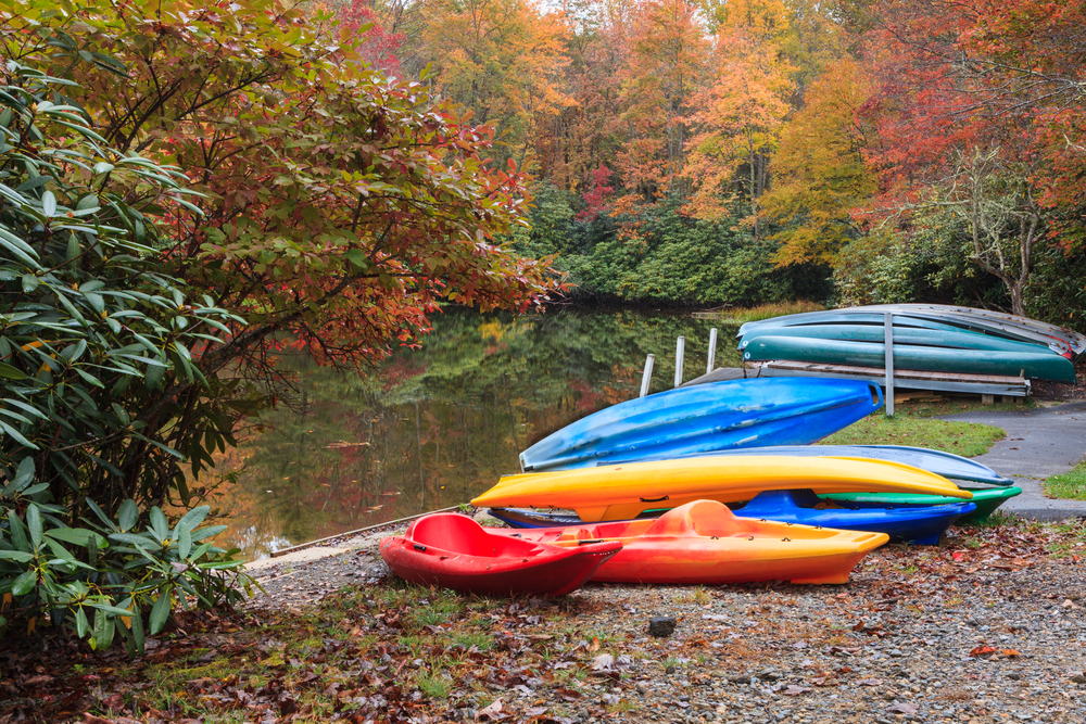 colourful kayaks resting on the side of the river in a beautiful fall landscape; one of the best things to do in Cherokee is enjoy nature!
