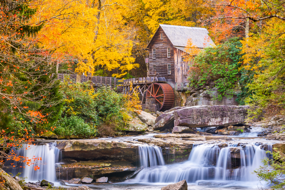 among the most popular things to do in west virginia, an old mill sits on a river surrounded by trees in the fall