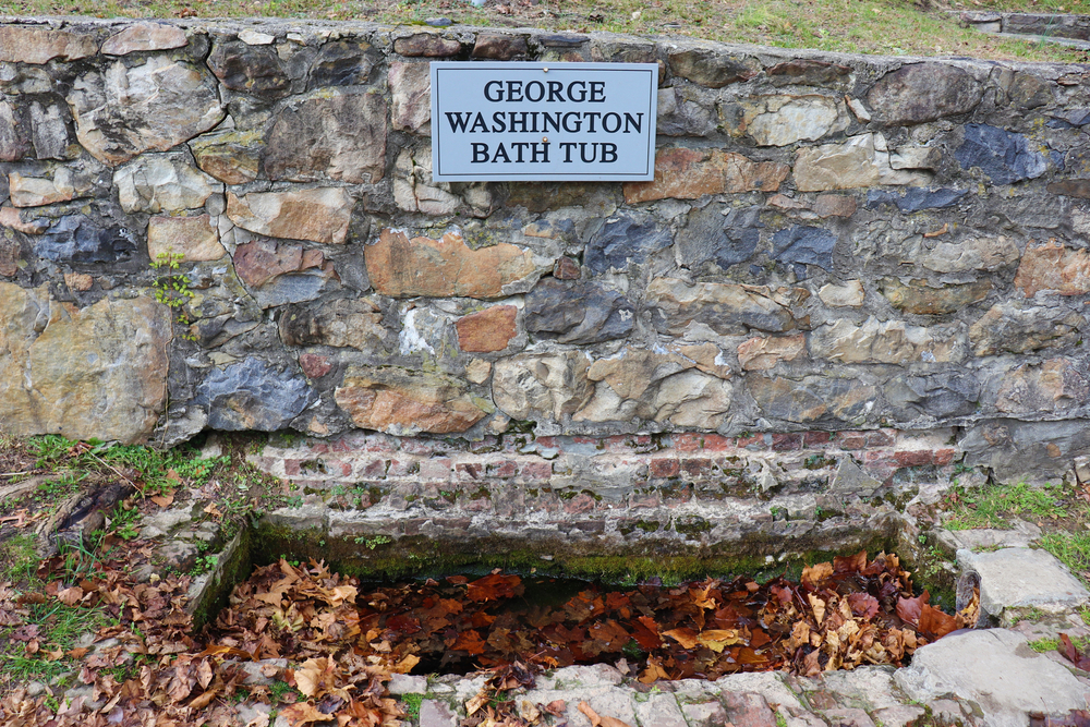 a rock wall holding a sing that says george washington bathtub with a small stone bath tub below it 