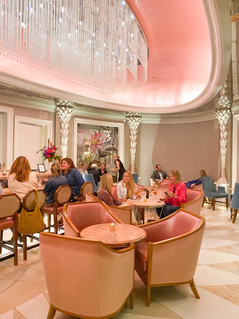 People seated inside Camellias, a bar with pink furniture and a crystal chandelier.