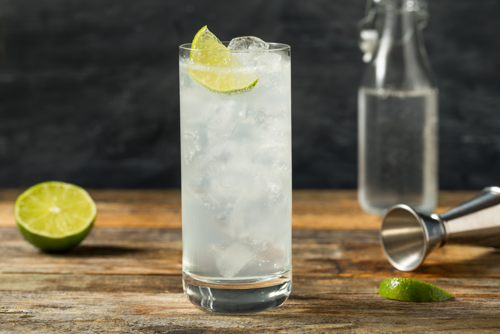 a glass of ranch water with a lime sits on the wooden bar, a lime and bottle sit behind it