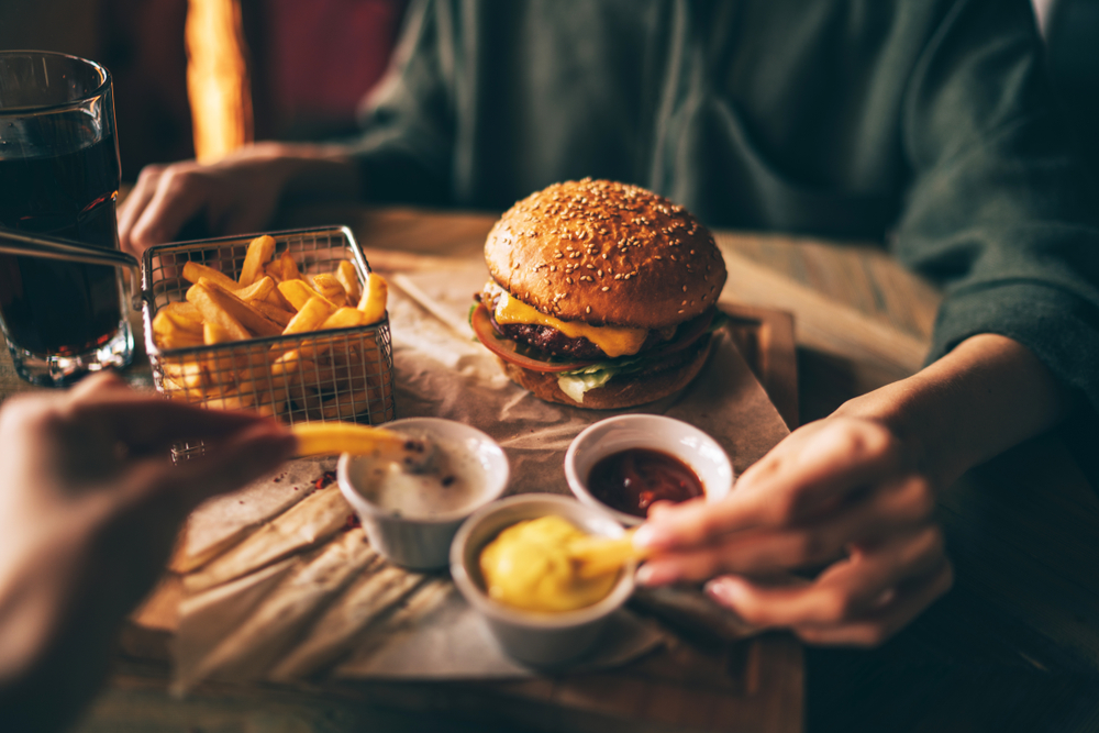 a burger and fries on the table with three dipping sauces and a glass with brown liquid in it