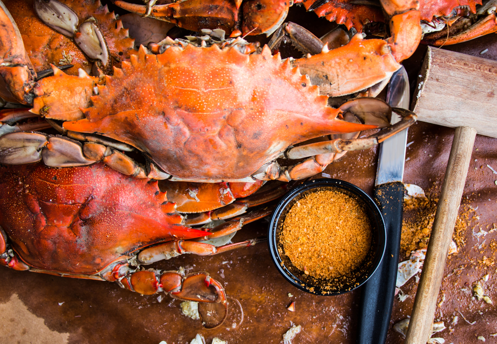 crabs on a table with a mallet and knife for opening them, a small bowl of seasoning is also on the table 