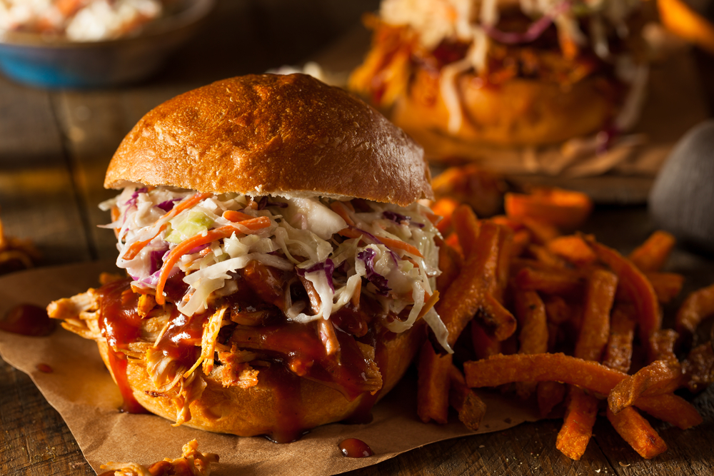 a pulled pork sandwich with cole slaw on it next to french fries, another burger and fries are in the background
