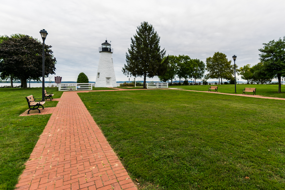 a cloudy day in a park, brick walk way on the left with benches along it and a small lighthouse in the back, one of the best small towns in maryland, havre de grace