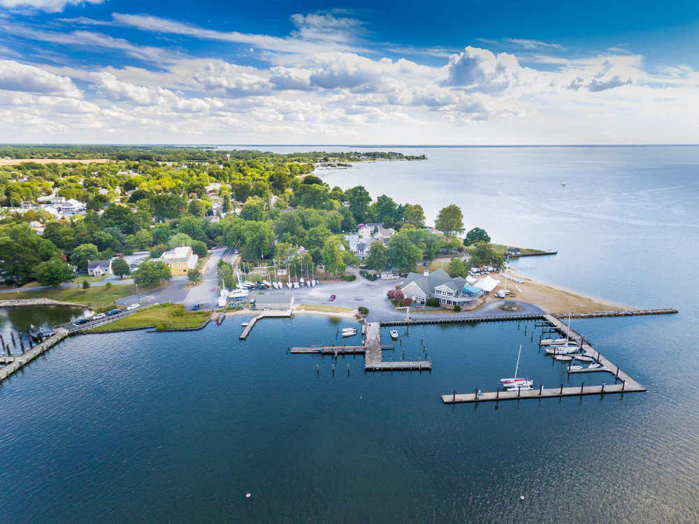 aerial photo of a town on the waters edge, a beach on the right and docks for boats in the middle