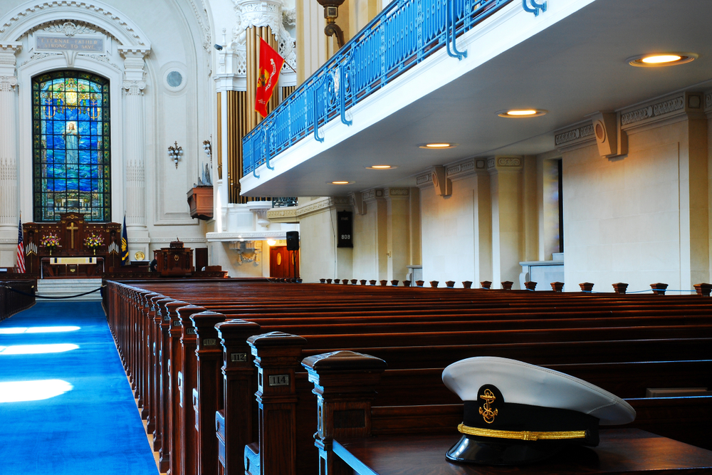 a naval hat sits in the foreground, pews on the right and a balcony, stained glass window on the left