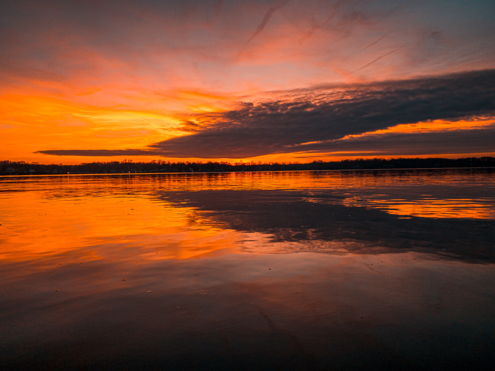 view over the water at sunset, clouds in the sky and trees in the background