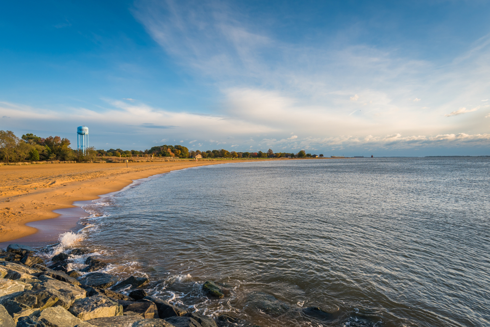 a curves sandy beach and water, a water tower is in the background on the left, sandy point state park, one of the best things to do in annapolis