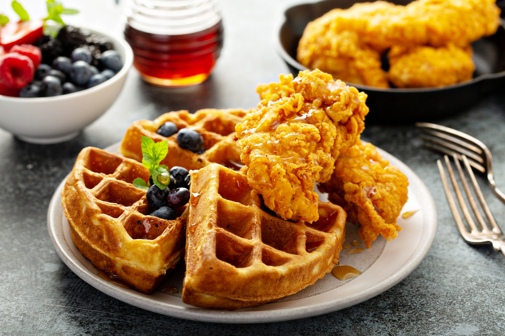 Three crispy waffles sit under two chicken tenders and syrup in this photo-- chicken and waffles will always be some of the best brunch in Atlanta. 