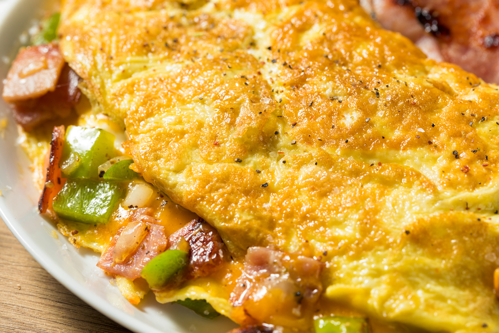 Photo of a delicious omelete from Charmed. This omelete has bacon, cheese, green bell peppers, and onions. 