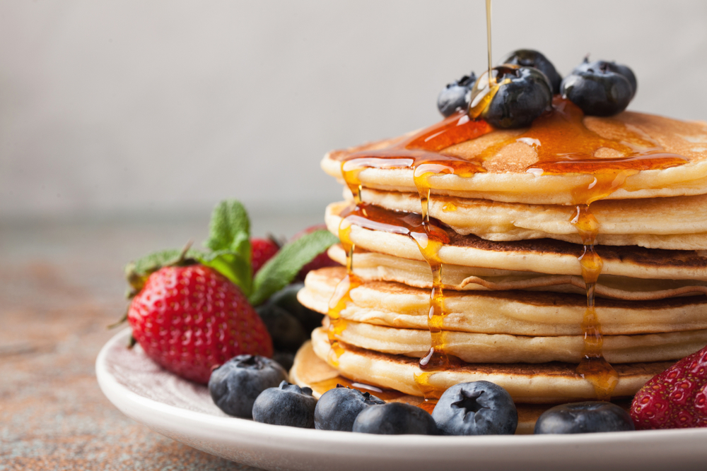 Stack of pancakes with blueberries and strawberries, and a drizzle of maple syrup from Snooze An A.M. Eatery.