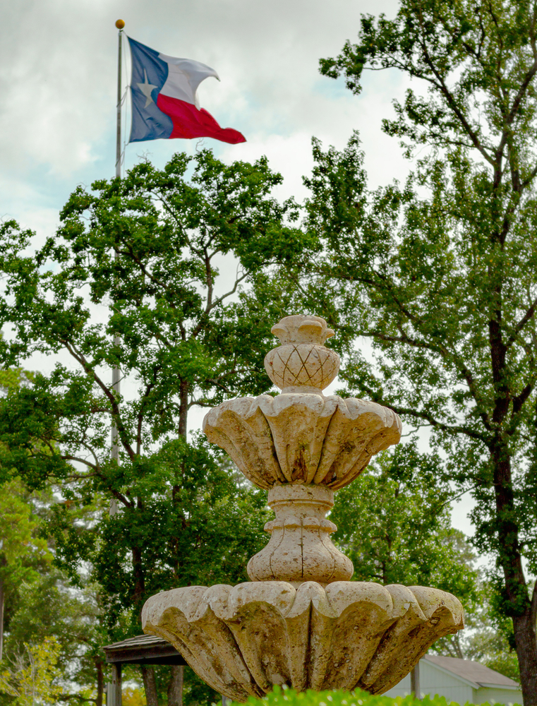 Photo of a fountain, with a Texas flag flying from a pole above the trees at the hesitate museums, one of the best things to do in Conroe 