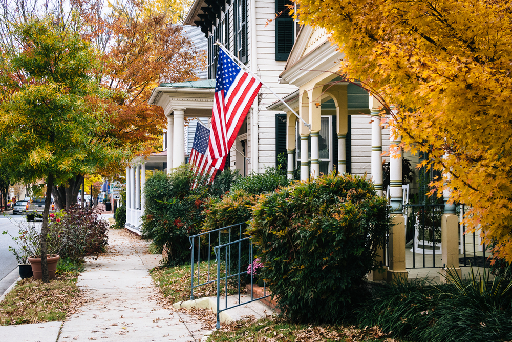 tree lined street with houses on the right, flags flying outside the houses and plants around the houses , easton, one of the best small towns in maryland 