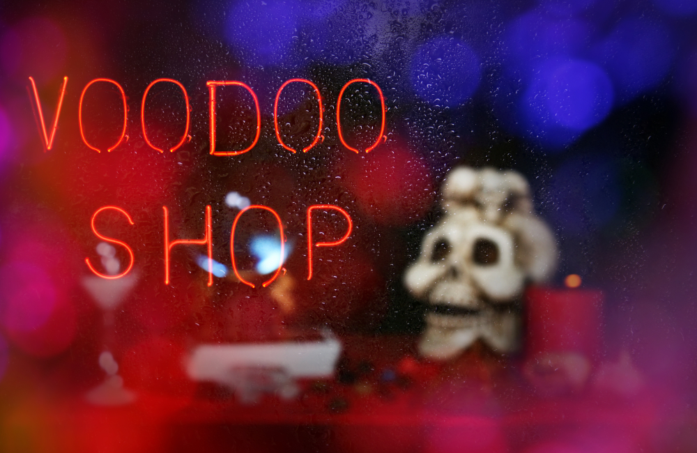 The neon sign in the window of a voodoo shop with water droplets on it. In the background you can see a skull and some candles