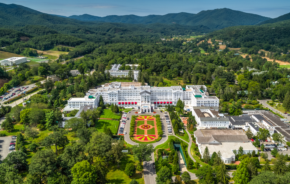 aerial photo of the greenbrier, one of the best weekend getaways in west virginia, flowers in an oval shape sit in front of the resort, trees and mountains behind it