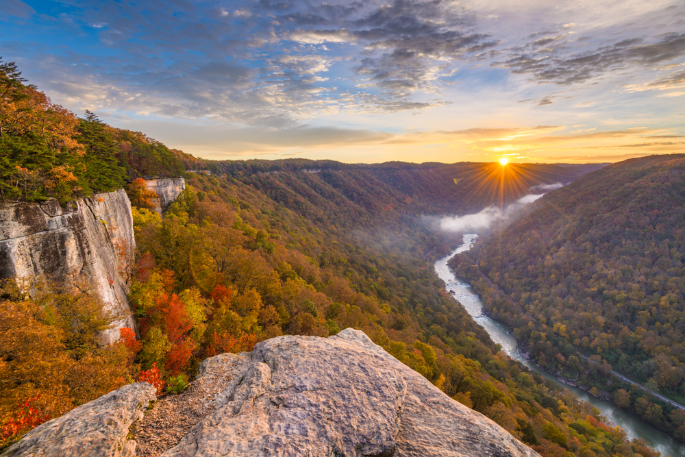 sunset over the mountains at the new river gorge, a river on the middle/right and a rock ledge on bottom of the picture