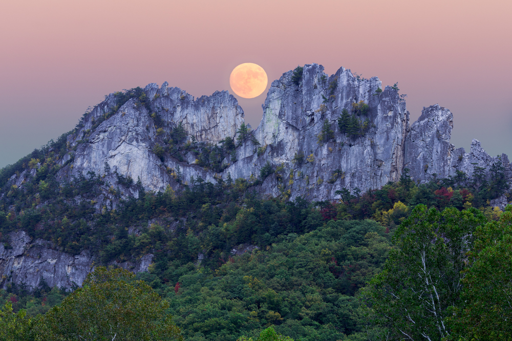 rock formations on mountains, trees below it and a full moon above