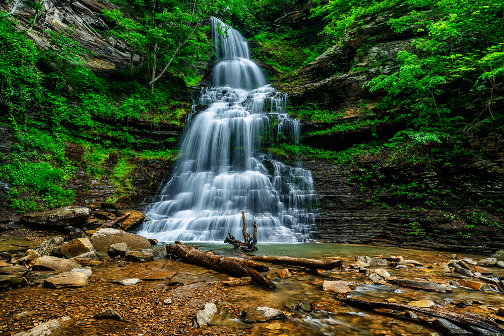 a waterfall in the woods falling down layered rock to a pool of water below