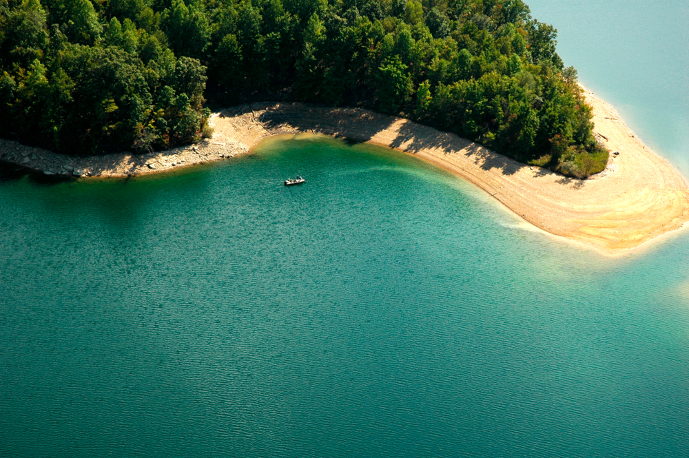 aerial photo of a lake and sandy shore with trees in the top of the picture