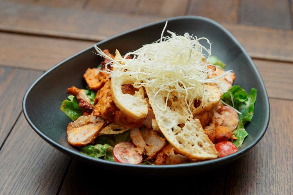 a grilled chick salad in a triangle shaped bowl with large croutons on top 