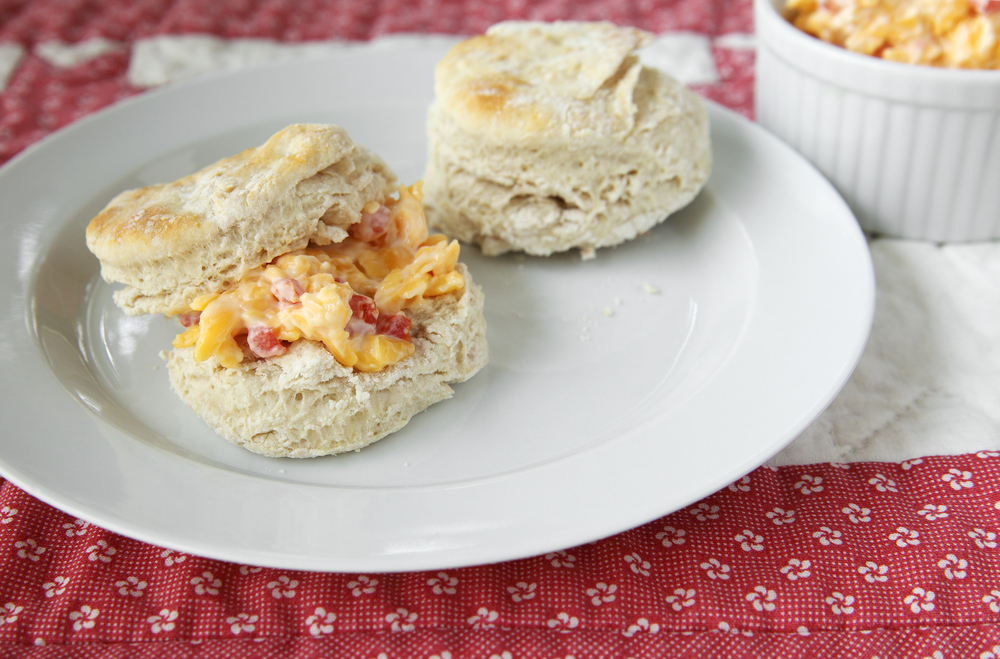 two biscuits on a plate, one of the biscuits has pimento cheese in between two halves of the biscuit