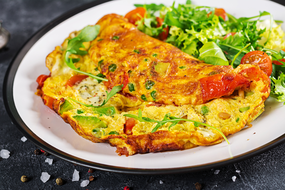 an omelete and a salad are on a round plate on a table, there are vegetables in the omelete