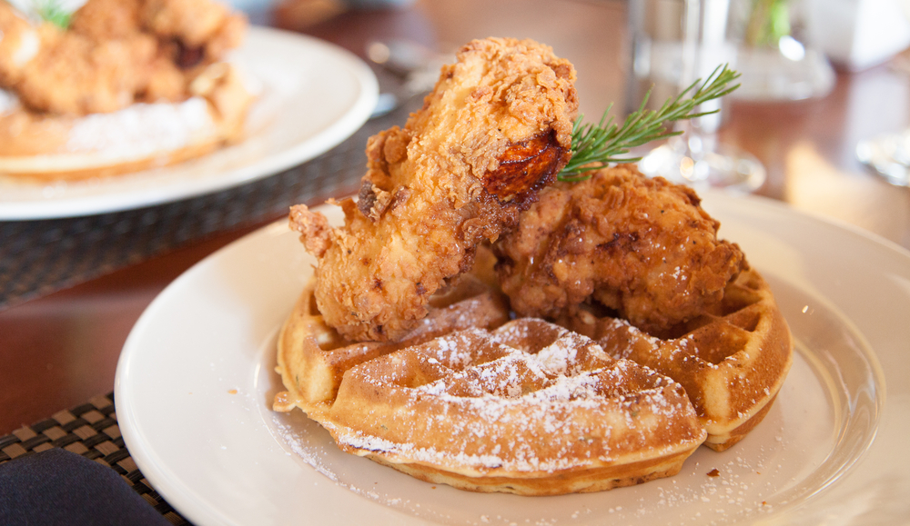a plate of waffles and chicken sits in the fore ground and another plate sits in the background. 