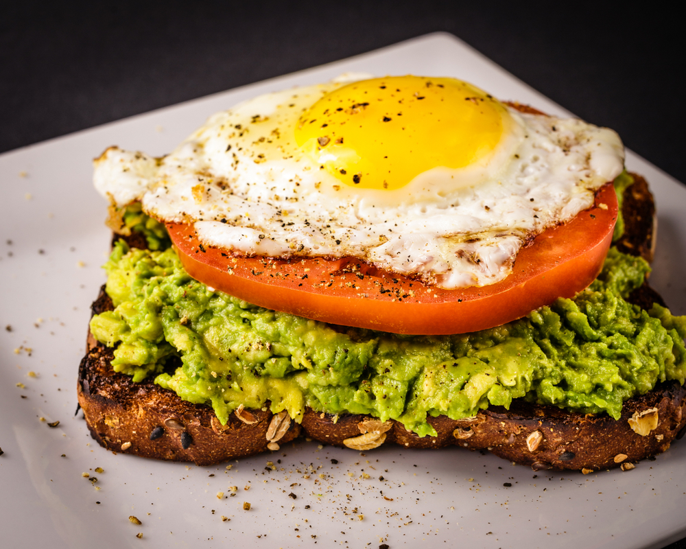avocado toast with tomato, egg, and seasoning on top
