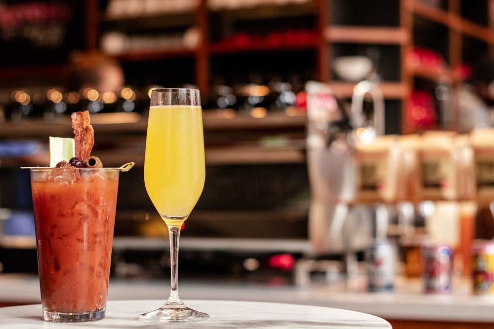 a bloody mary and a mimosa sits on a table in front of the bar