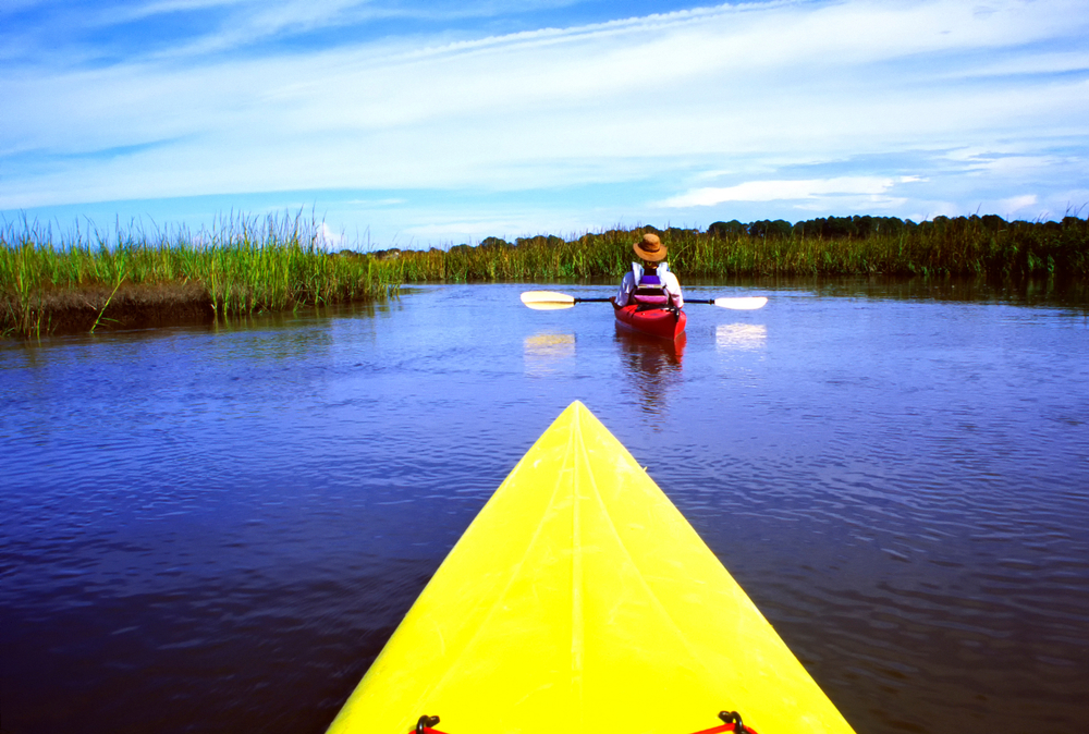 kayaking in the blue water with a yellow kayak with a lady in front in a red kayak 