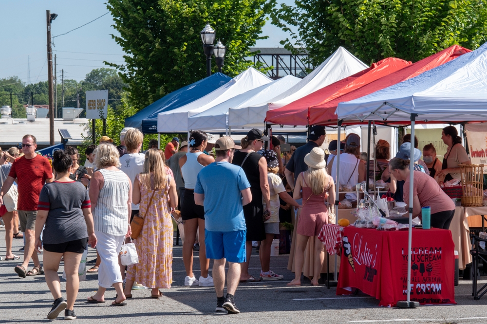 people walk around a framers market in marietta, tents are set up selling produce and goods on the right 
