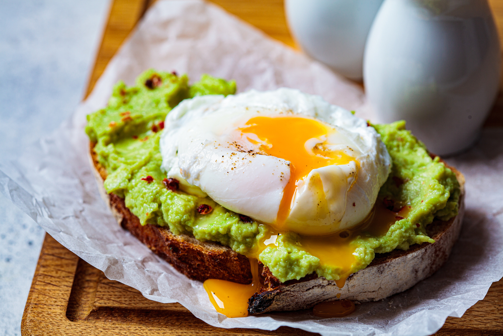 A slice of avocado toast with a poached egg on top oozes yolk onto a plate at a one of the top locations for best brunch in Charlotte.