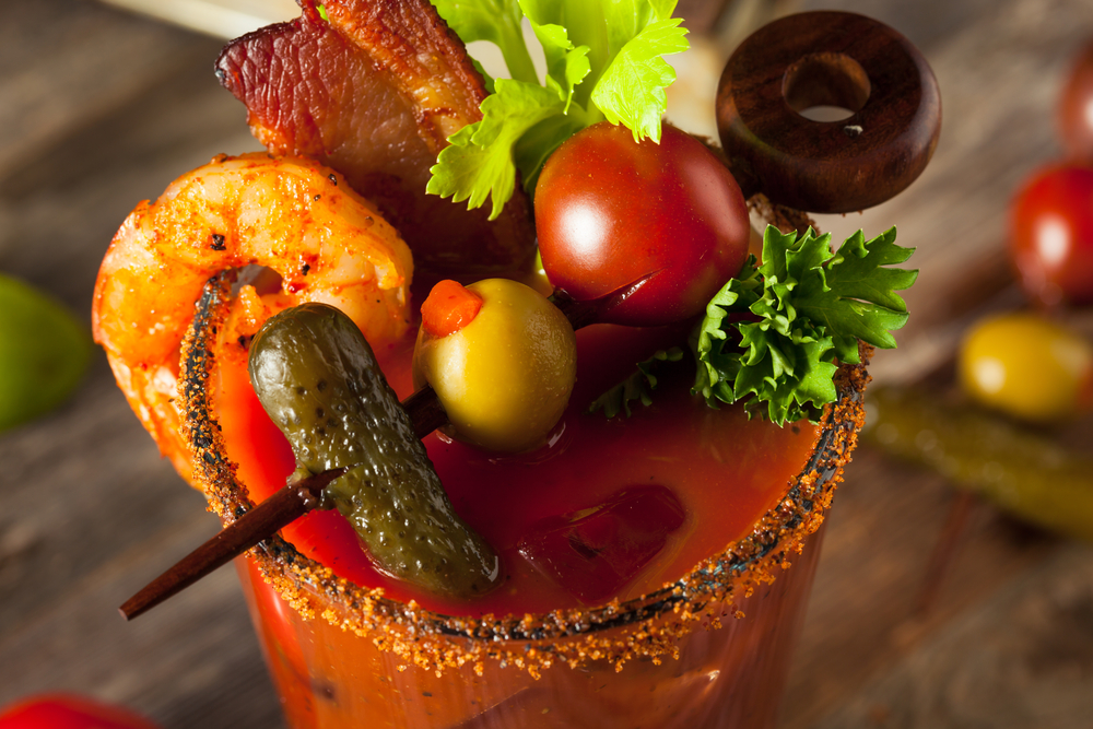 A zoomed in photo shows the top of a bloody Mary, which is adorned with shrimp, bacon, pickles, olives, and tomatoes, making it one of the best cocktails at the best brunch in Charlotte. 