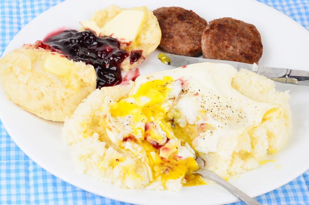 A classic combo of butter grits and eggs, with a buttered biscuit and sausage sits on a white plate, making It a classic and yet one of the top options for the best brunch in Charlotte. 