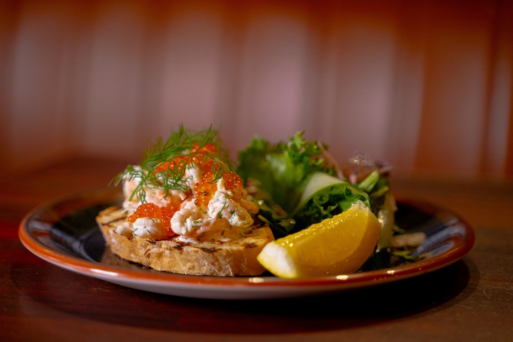 This crawfish sandwich is spread across toasted bread and features a sliced lemon and dill on top.