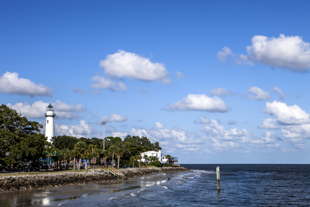 the pretty light house in st Simon island in ga with a shore and rocks along the coast 