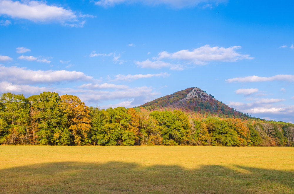 The sun shines on Pinnacle Mountain State Park during early fall, with leaves beginning to change color. This will be a good location to watch the Arkansas Solar Eclipse.