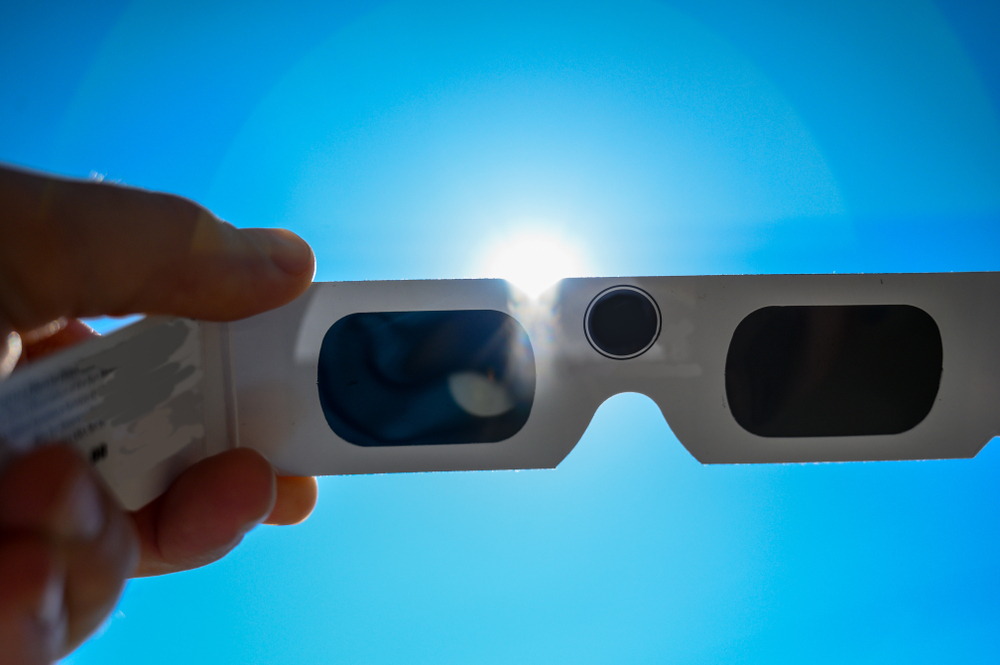 A hand holds up a pair of specially-made eclipse glasses against the sun, which must be worn during the Arkansas Solar Eclipse.