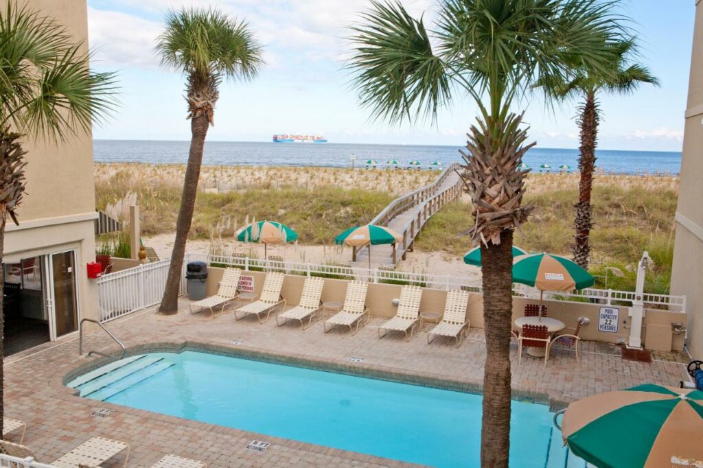 The pool area at the Desoto Beach Hotel with palm trees and a boardwalk leading to the beach.