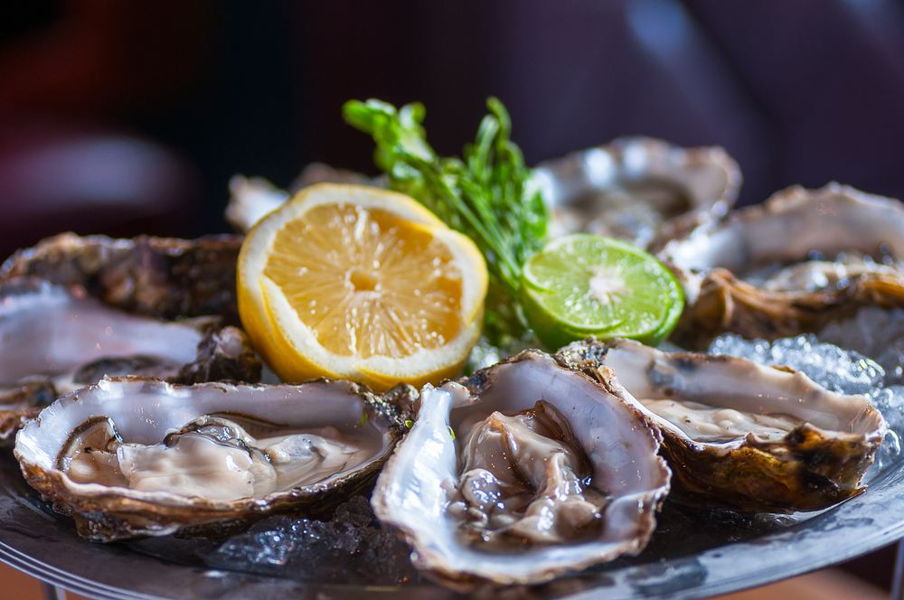Oysters sit on a bed of ice with lemon and lime in the center of the tray.