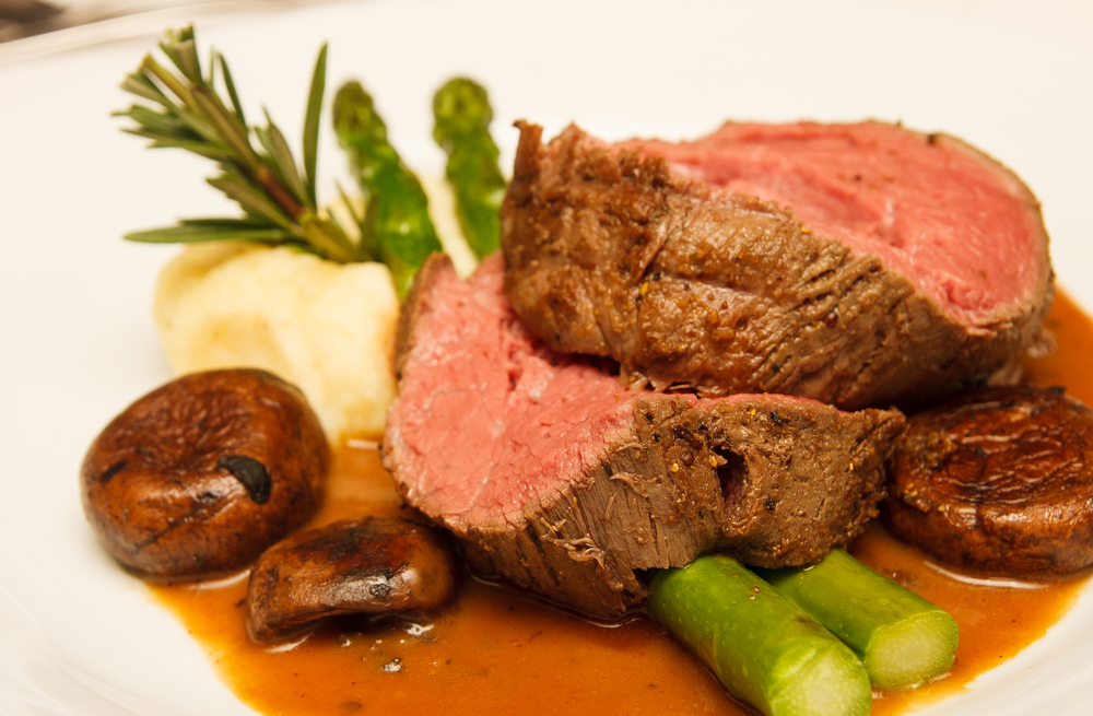 Rare-cooked prime rib sits on a white plate with asparagus, mushrooms, and mashed potatoes, like that served at Billy's, one of the best restaurants in Roanoke.