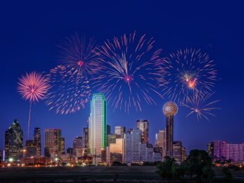 The skyline of Dallas is light up at night, with great fireworks bursting above, showing some insight to some of the best things to do in Dallas at night!
