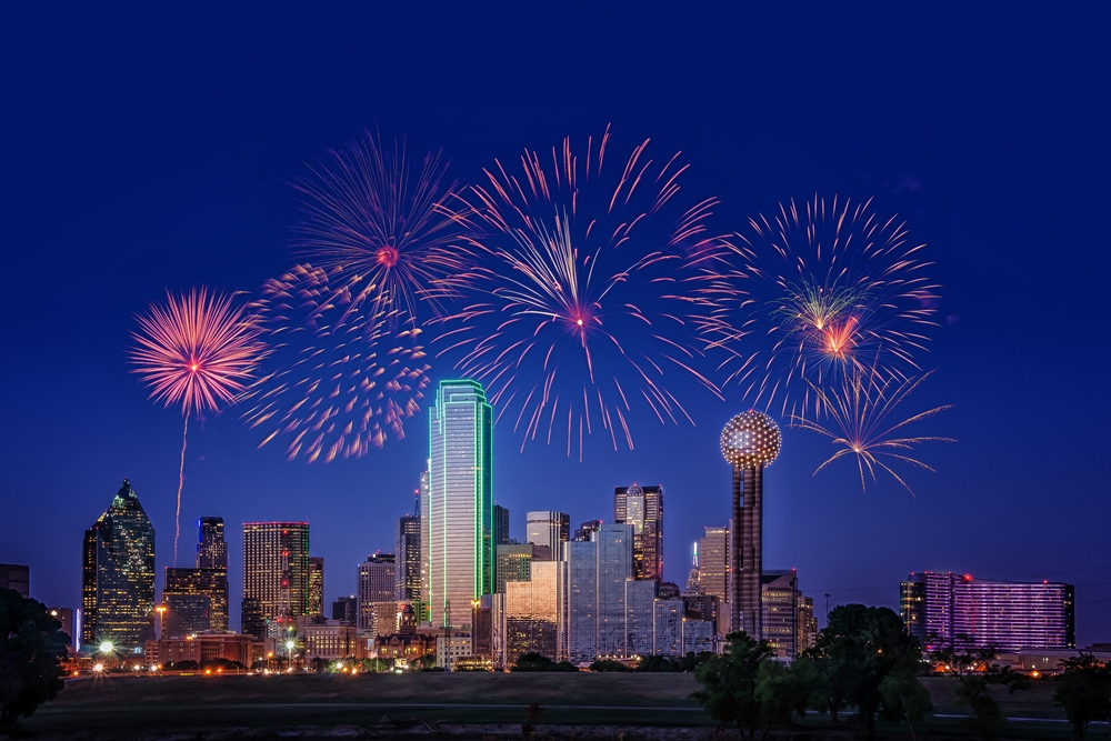 The skyline of Dallas is light up at night, with great fireworks bursting above, showing some insight to some of the best things to do in Dallas at night!