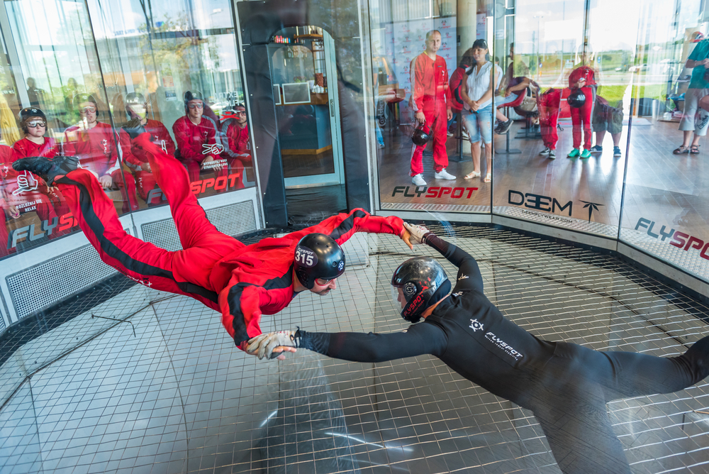 A guide and a gentleman fly in a tunnel of wind, participating in indoor skydiving, which is one of the best things to do in Dallas at night.